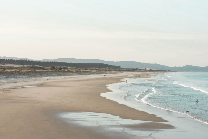 a beach shot showing a length of shoreline with 2 people on it